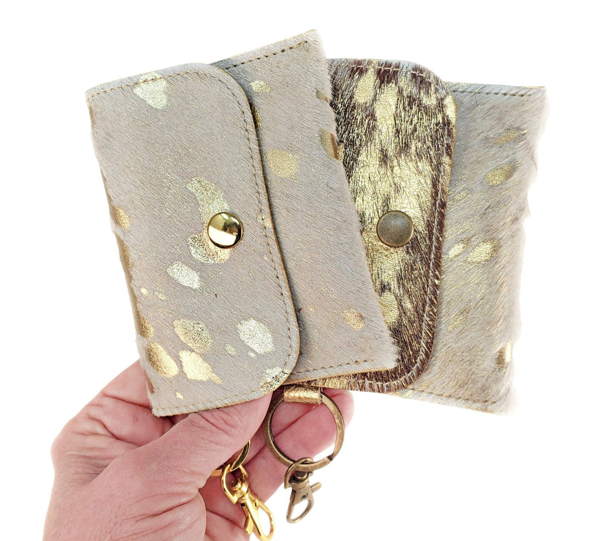 Three acid-wash cowhide keychain wallets in neutral gold and brown finishes with snap closures and metal clips